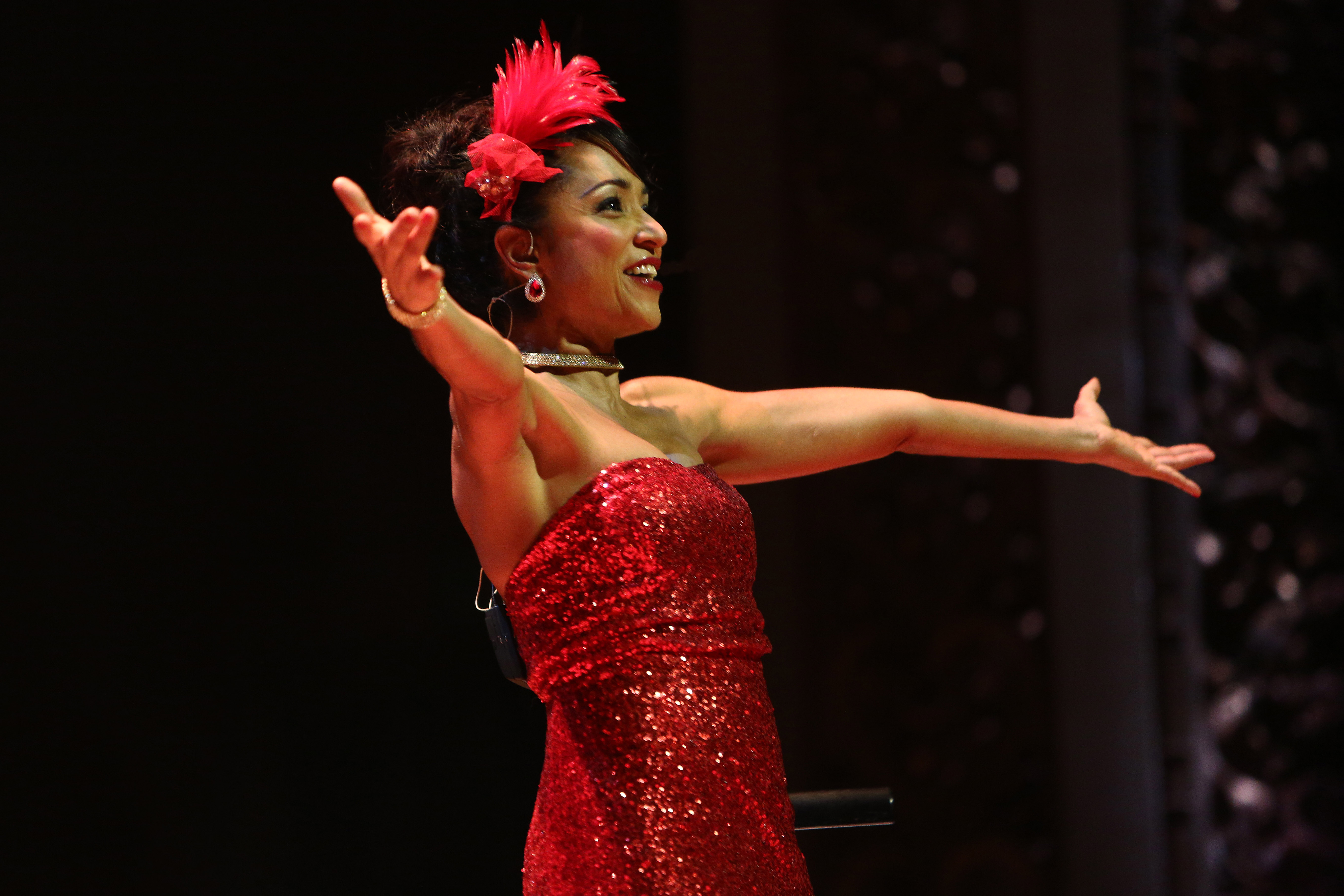 Spectacle "Joséphine Baker - Paris, mon amour" La Rampe 2020 Une chanteuse / danseuse est sur scène. Elle porte une robe rouge à paillette. Elle écarte les bras face au public.