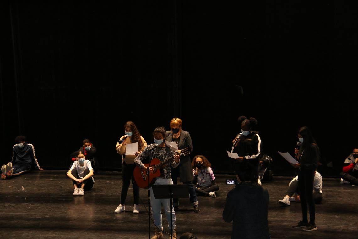Des jeunes masqués présentent un spectacle de musique (chant, guitare) sur la scène de la Rampe