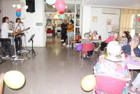 Photo prise à la fête de l'été de la Résidence autonomie Maurice-Thorez. Nous voyons les résidant-es seniors assis autour de tables rondes. des ballons colorés sont suspendus au plafond. Les résidant-es assistent à un spectacle de musique.