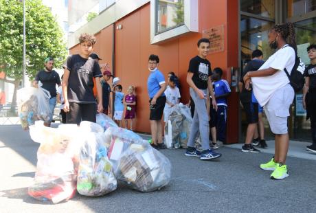 Photo prise dans le cadre de l'opération Ville propre.  Nous voyons des bénévoles, équipées de  gants, de pinces et de sacs. Ils amènent les sacs de déchets ramassés au point de collecte.