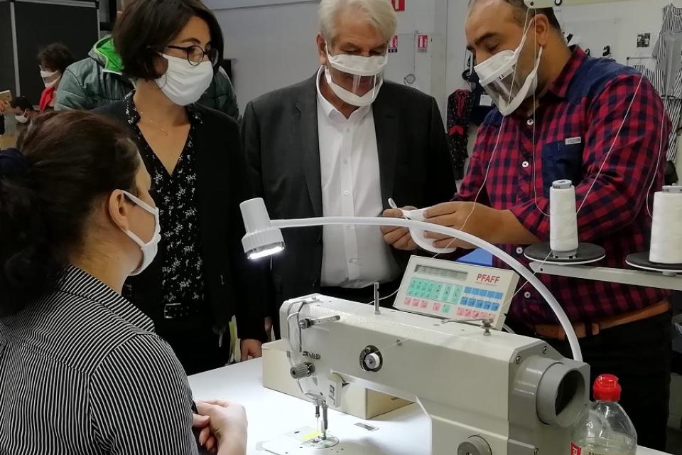 Guidés par Hamid, chef d'atelier, la première adjointe Amandine Demore et le maire REnzo Sulli découvrent les différentes étapes de confection des masques inclusifs, devant le poste de travail d'une couturière. 