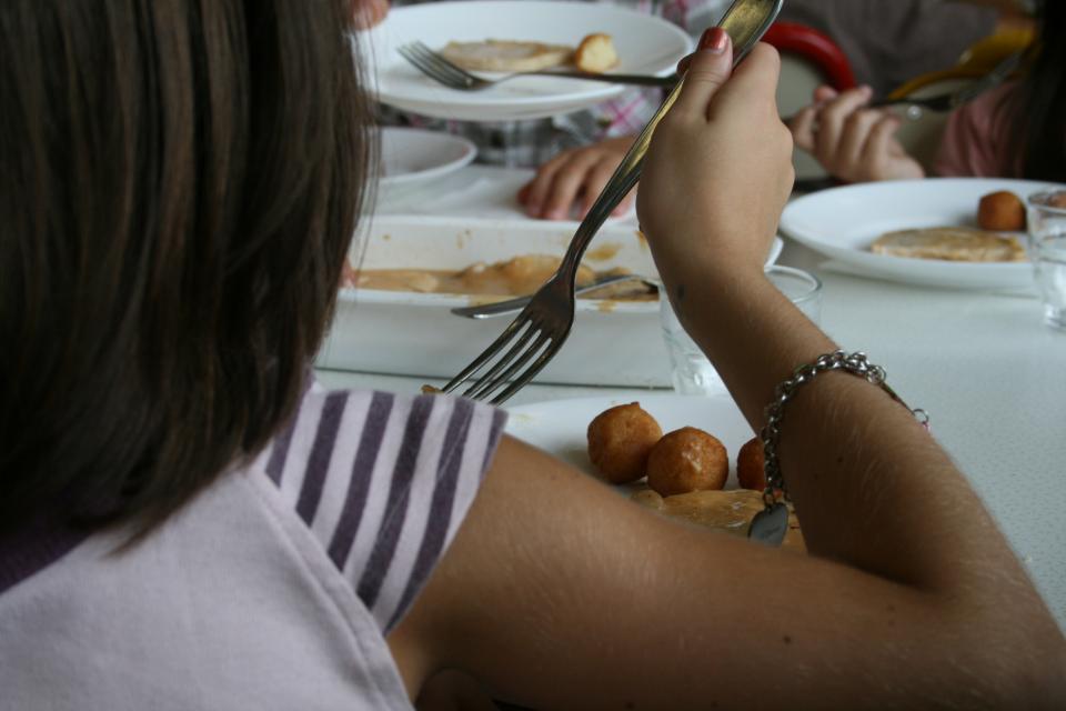 Vue de dos sur une petite fille qui mange à la cantine. Elle est assise à une table et mange.