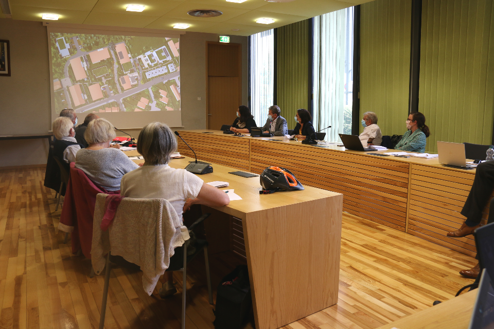 Photo prise en salle du conseil municipal. Les élu-es présentent le projet aux habitant-es sur un écran.
