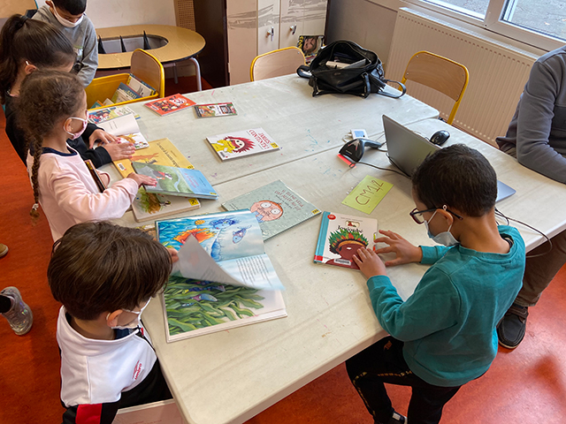 Plusieurs enfants sont autour d'une table. Sur celles-ci plusieurs livres sont à leur disposition.