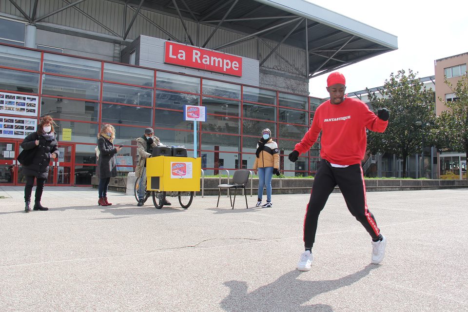 Alan, danseur du groupe Soo7kill, danse sur le parvis de La Rampe, le triporteur de La Rue des cultures en arrière plan.