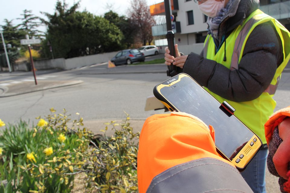 Cartographie interactive : Le bon plan ! Vue sur deux agentes de la Ville qui effectuent un relevé précis des modifications apportées à la voirie, aux espaces verts, au petit mobilier, marquage au sol, panneaux de signalisation. Elles sont équipées d'un GPS situé au sommet d'une perche de géomètre et d'une tablette qui enregistre les informations recueillies.
