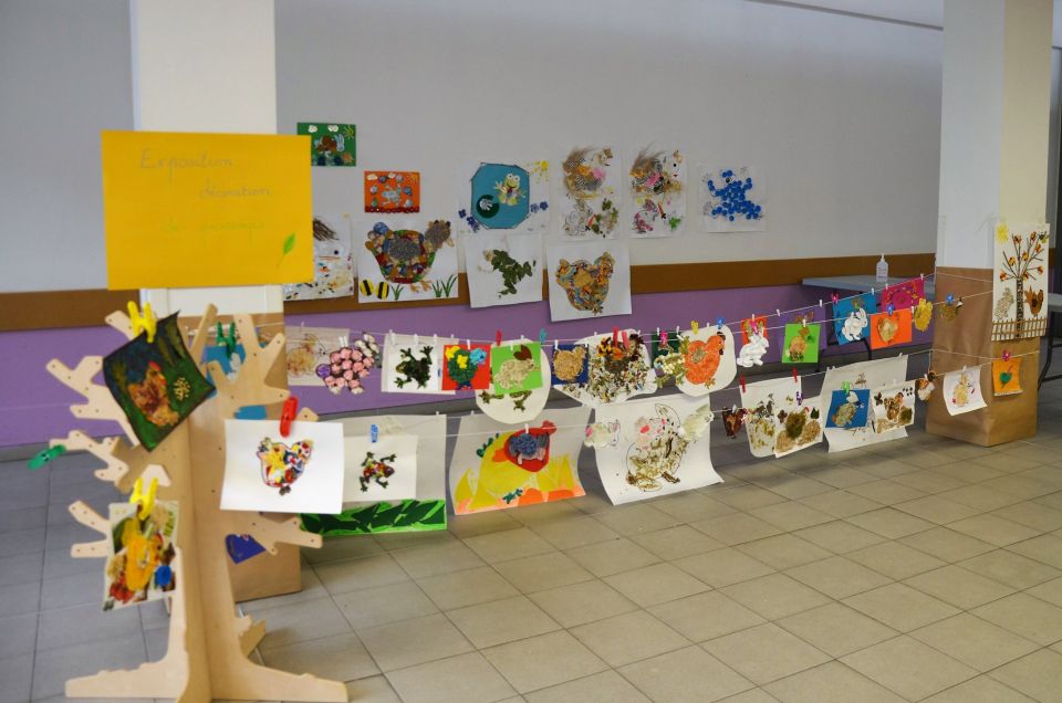 Exposition éphèmère du Ram Photo de la salle d’Estienne d’Orves. Des fils sont étendus entre les poteaux et nous voyons des dessins d'enfants exposés, accrochés aux fils avec des pinces. Certains sont affichés aux murs.