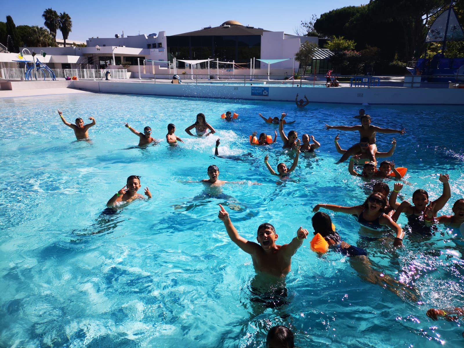 Photo prise au centre de vacances de la Grande Motte. Nous y voyons pleins d'enfants dans la piscine qui jouent, s'éclaboussent. Certains ont des brassards d'autres non.