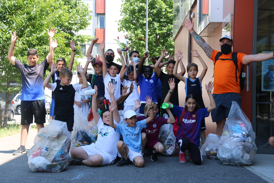 Au village 2, plusieurs groupes d'enfants ont nettoyé le quartier. Photo prise dans le cadre de l'opération Ville propre. Nous voyons des bénévoles, équipées de gants, de pinces et de sacs. Ils posent côte à côte.