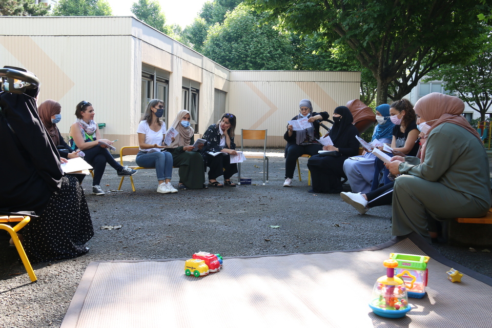 Le temps d'échange entre parents à l'école Elsa Triolet Photo de parents assis en cercle sur des bancs dans une cour d'école.
