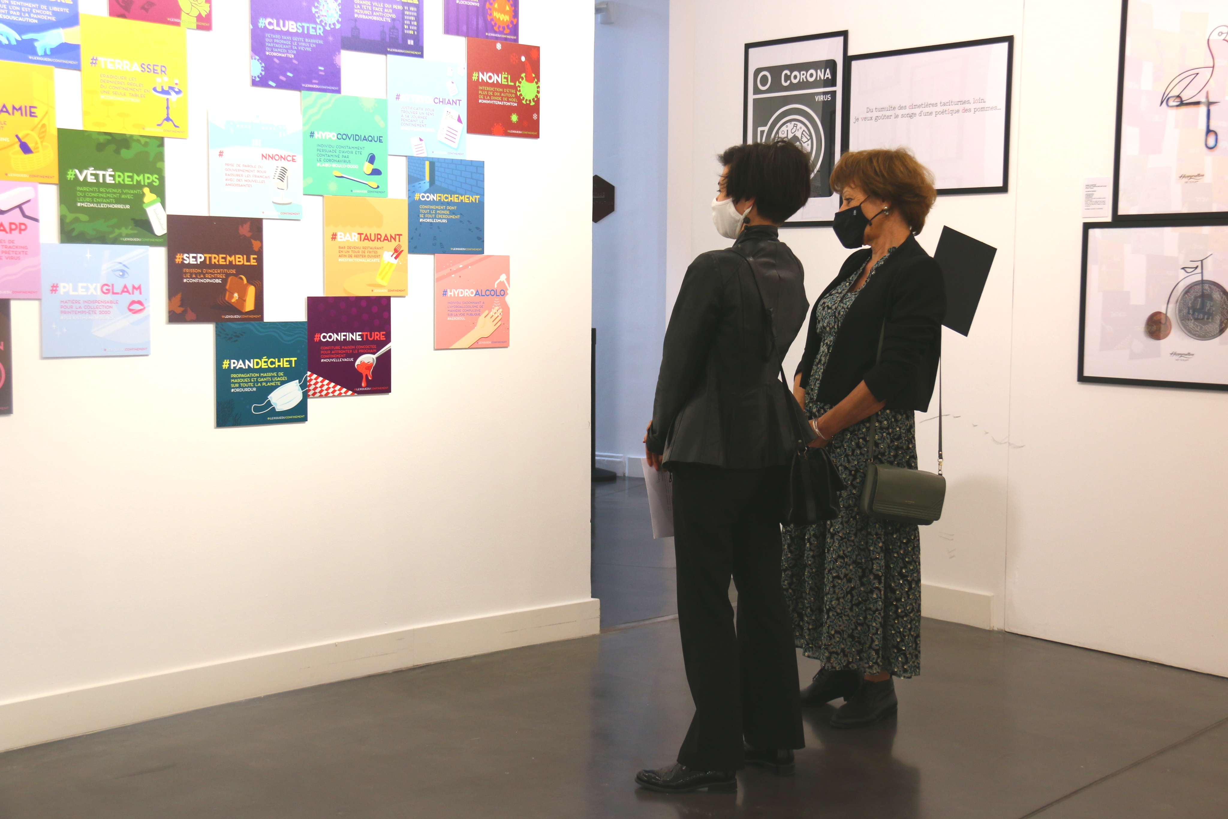 Photo de l'exposition "L’art déconfiné des confinés" au centre du graphisme. Virginie Vignon, la conservatrice et Jacqueline Madrennes, adjointe à la culture, lisent le “Lexique des confinés”. Il s'agit de mini affiche très colorées et visuelles, expliquant certains " mots mêlés" comme "impuichiant".