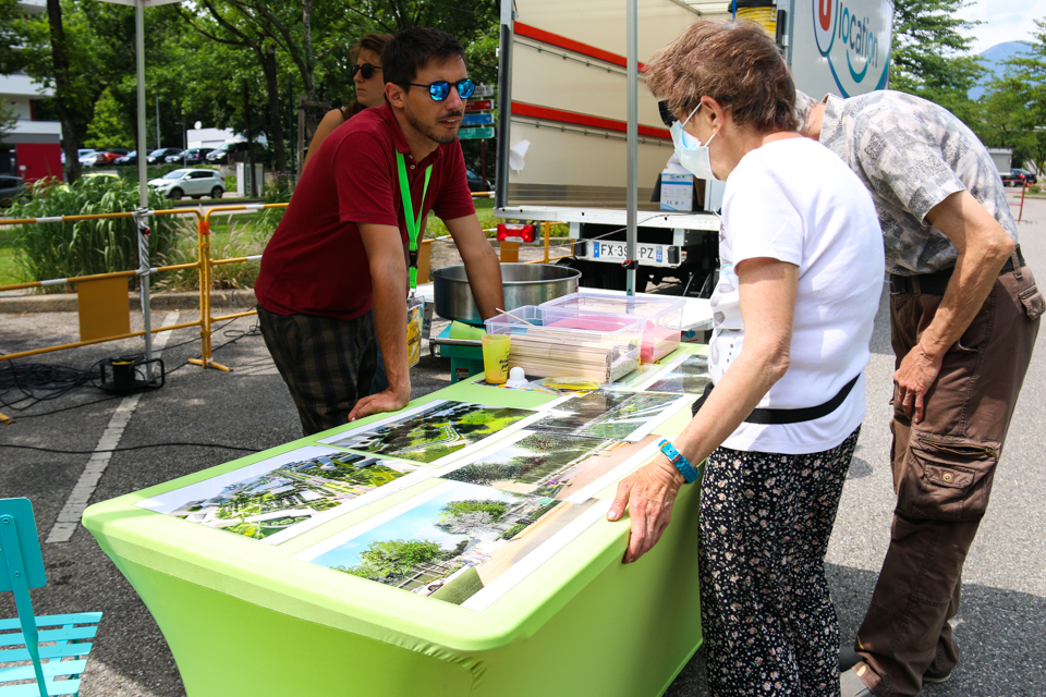 Un agent présente le projet urbain qui va modifier le quartier à des habitant-es.  Il leur montre des photos simulation de ce que sera le quartier après les travaux.