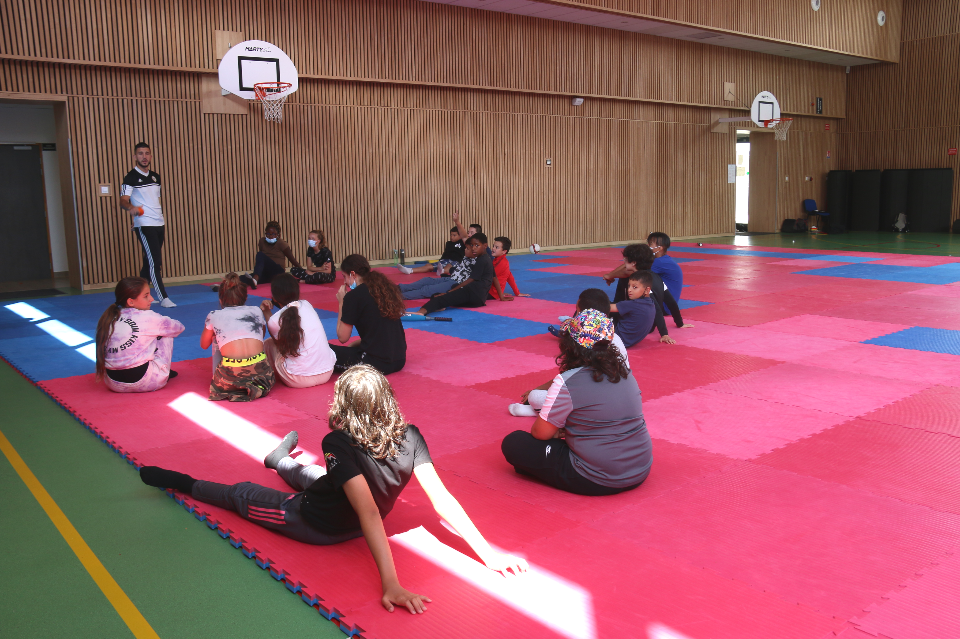 Atout sport Boxe 2021 Photo prise avant une activité sportive. Des jeunes garçons et jeunes filles sont assis sur des tapis et un éducateur sportif se tient debout face à eux et leur explique les consignes.