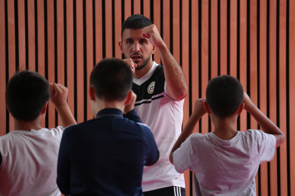 Un éducateur sportif au club de boxe d'Échirolles apprend la bose à 3 jeunes garçons. Il leur montre le bon positionnement des bras pour se défendre et les jeunes l'imitent. 