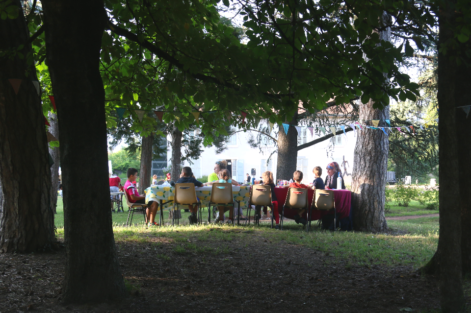 Photo d'un atelier artistiques. Une animatrice accompagne une dizaine d'enfants assis autour d'une table.