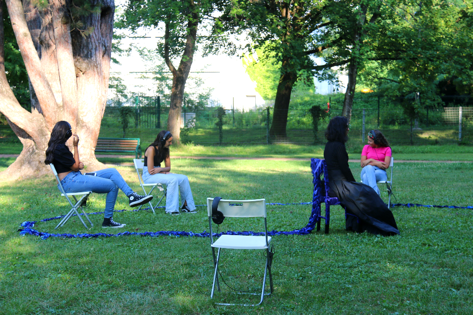 Expérimentation sonore. Des jeunes filles sont assises sur des chaises dans un parc, elles ont des casques sur les oreilles.
