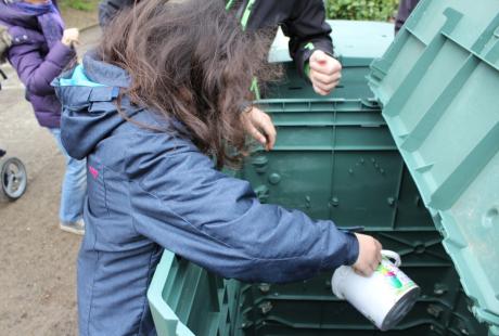 Une jeune fille prend du compost dans un composteur
