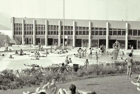 Vue en noir et blanc du stade nautique en 1972. Un groupe de jeunes se prélasse dans l'herbe.  Des familles sont installées au bord de l'eau. 