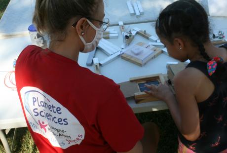 Une animatrice accompagne une jeune fille dans la réalisation d'une expérience scientifique.