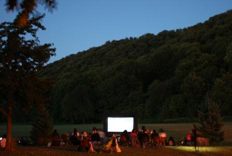 Une grande toile blanche est installée au milieu du parc. Le public s'installe en vue de la projection nocturne.