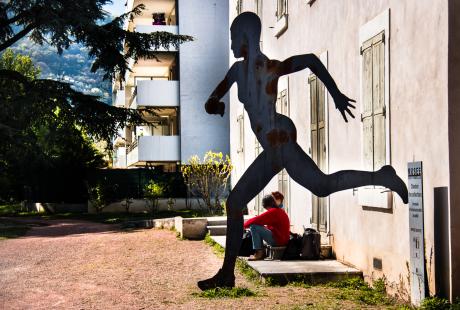 Marie Mazille et Fabrice Vigne, deux musiciens compositeurs sont assis sur une marche du Musée Géo-Charles. La photo est prise de loin. Dans un effet d'optique, on les aperçoit comme étant assis sous la jambe, levée en arrière, de la statue