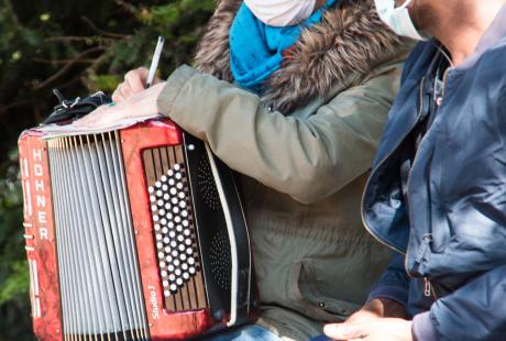 Photo de Marie Mazille et d'un habitant. Ils sont assis sur un banc et discute. Marie tient son accordéon et écrit une chanson