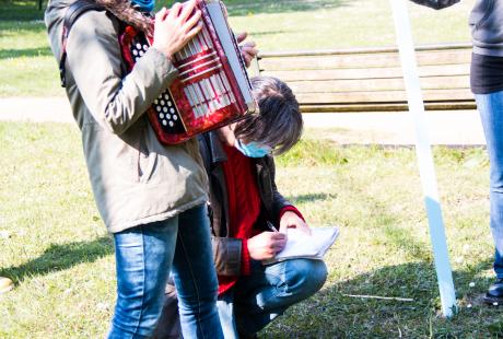 Marie Mazille est debout et tient son accordéon. Fabrice Vigne est agenouillé à côté d'elle et écrit une chanson.
