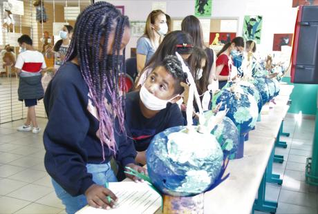 Photo prise dans le cadre du Projet Philo-plastique. Nous voyons des maquettes de la terre réalisées avec du plastique pour sensibiliser aux enjeux écologiques. Des jeunes regardent ces maquettes et discutent à leur sujet et au message qu'elles sont censées transmettre.