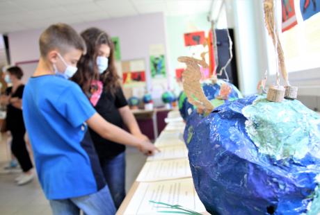 Photo prise dans le cadre du Projet Philo-plastique. Nous voyons des maquettes de la terre réalisées avec du plastique pour sensibiliser aux enjeux écologiques. Des jeunes regardent ces maquettes et discutent à leur sujet et au message qu'elles sont censées transmettre.