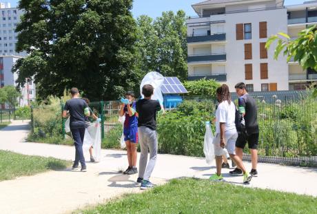 Photo prise à l'occasion de l'Opération Ville propre sur le secteur Village 2. Nous voyons une équipe de bénévoles composée de jeunes, ramasser des déchets. Ils sont équipés de gants, de sacs poubelles.