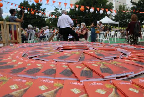 Photo de la présentation de saison la Rampe-La Ponatière pour la saison 2021-2022.  Des brochures de la saison 2021-2022 sont disposées en rond sur une table. En fond, flouté, nous apercevons les spectateurs.