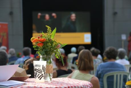  Photo de la présentation de saison la Rampe-La Ponatière pour la saison 2021-2022. Au premier plan un bouquet de fleur orange et blanc aux couleurs de la saison. En arrière plan, flouté, nous voyons le public regardant  la scène.