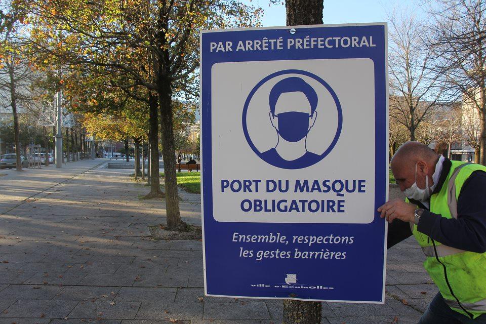 Un agent de la Ville pose un panneau indiquant le port du masque obligatoire.
