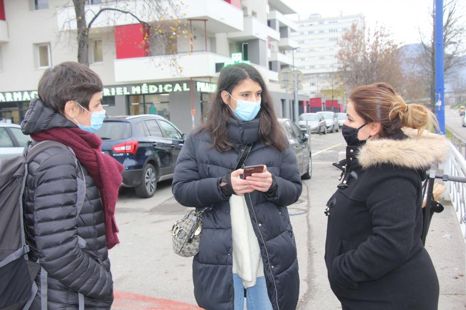 Une jeune femme interroge deux passantes sur leurs expériences du numérique. Elle tient à la main son téléphone pour récolter leurs témoignages.