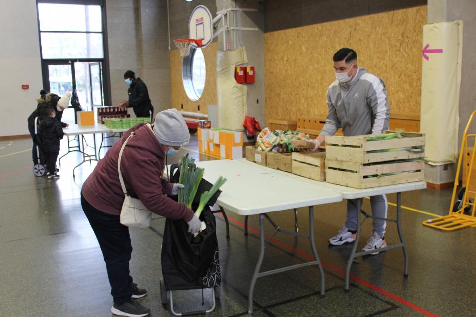 Vue sur une distribution alimentaire. Les jeunes bénévoles de l'association Human Helop sont derrière des tables sur lesquelles sont disposées des denrées alimentaires, qu'ils distribuent aux habitant-es.