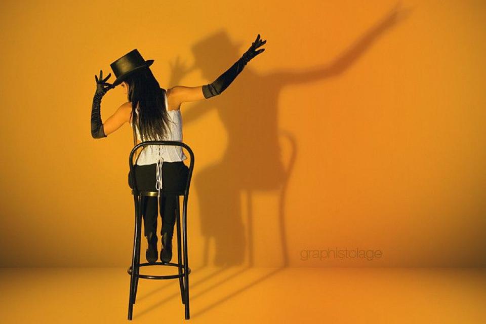 Evade se met au cabaret Une jeune Fille, habillée avec un haut blanc, un pantalon noir et un chapeau noir, est assises sur une chaise haute. Elle tient son chapeau par le bord, avec la main gauche et tend son bras droit en diagonal vers le haut.