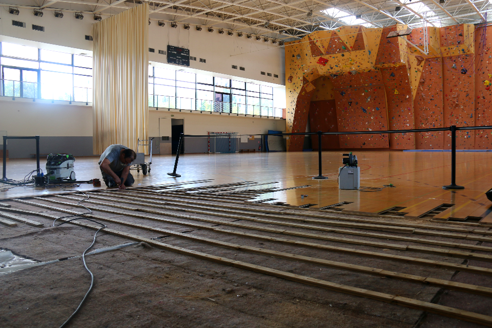 Les réparations du parquet du gymnase Lionel Terray Photo des réparations du parquet du gymnase Lionel Terray. La photo est prise dans le gymnase, nous voyons le mur d'escalade en fond. Au premier plan nous voyons un technicien en train de changer les lames du sol.