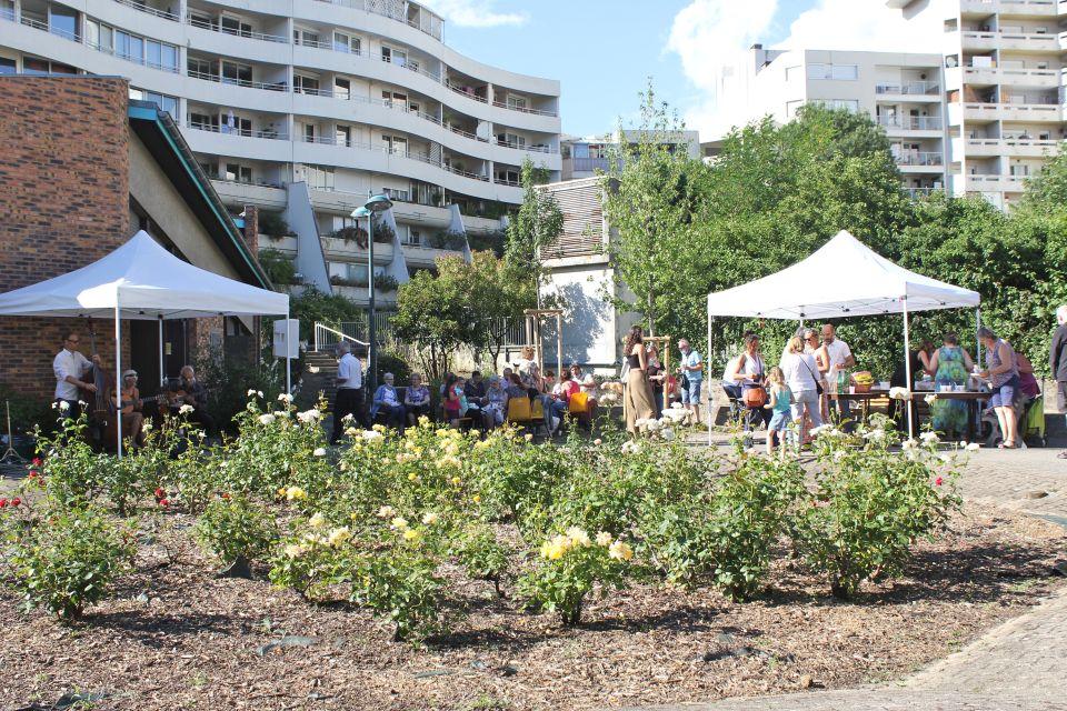 Photo prise devant la MDH Anne-Frank. Des tentes sont montées, des tables dressées. Des habitant-es échangent entre eux