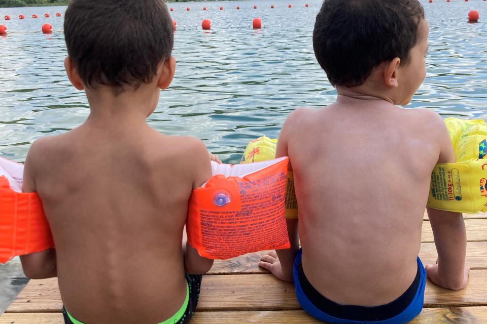 Les inscriptions sont encore possibles pour cet été ! Deux garçons avec des brassards assis devant un lac